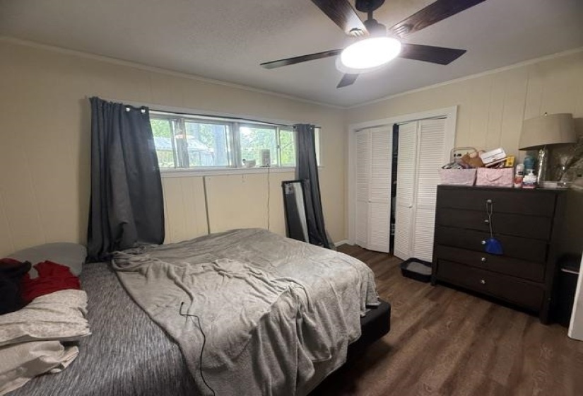 Bedroom featuring wood-finish flooring, a ceiling fan with integrated lighting, a horizontal window with dark drapery, and bi-fold closet doors