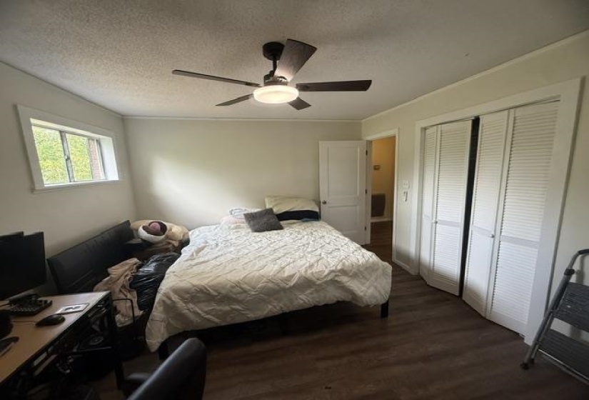 Room featuring wood-finish flooring, a ceiling fan with integrated lighting, a window with exterior views, and bi-fold louvered closet doors