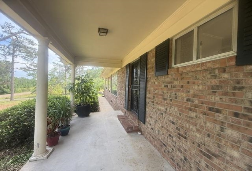 Expansive covered porch with a concrete surface, featuring classic white columns and a brick exterior