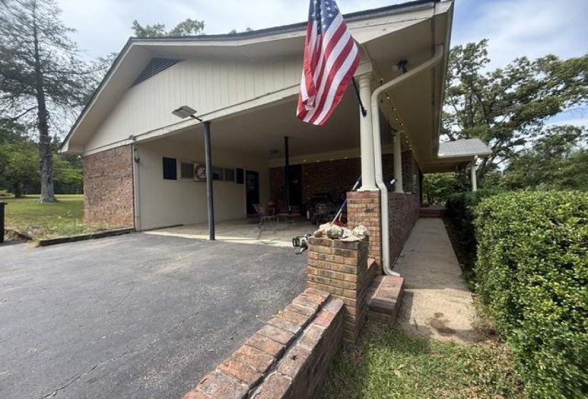 Brick exterior featuring a covered carport, paved driveway, and mature landscaping