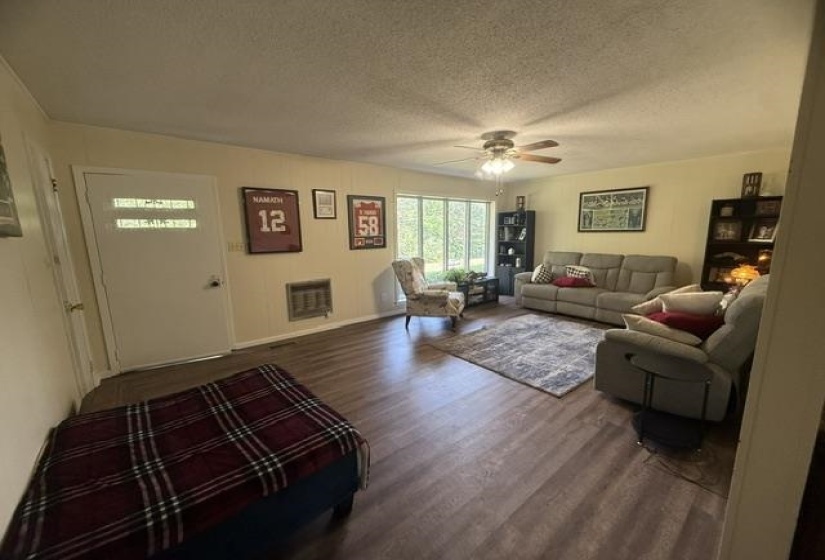 Spacious living area featuring wood-finish flooring, a ceiling fan with integrated lighting, and multiple large windows