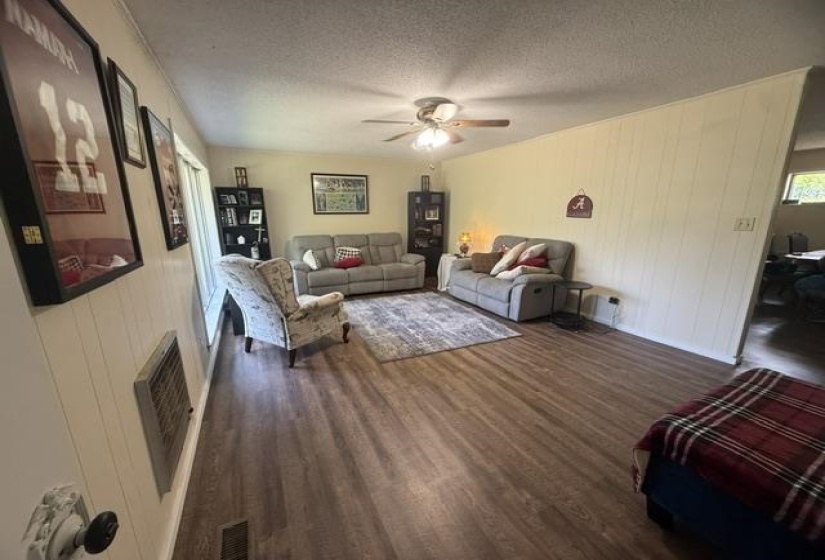 Spacious living area featuring wood-finish flooring, a ceiling fan, and paneling on one wall