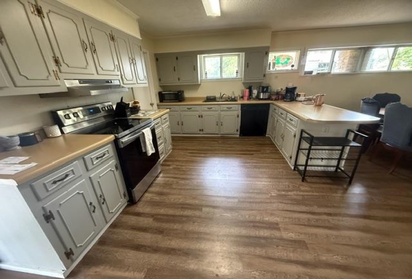 Spacious kitchen featuring extensive cabinetry, resilient wood-finish flooring, a built-in oven with overhead microwave, a stainless steel range hood, and a peninsula with seating