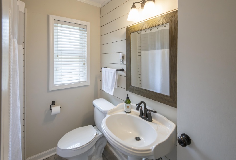 Bathroom featuring a pedestal sink, wall-mounted mirror with wood-finish frame, and modern light fixture