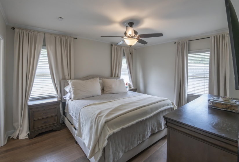 Bedroom featuring wood-finish flooring, two windows with blinds, and a ceiling fan with integrated lighting