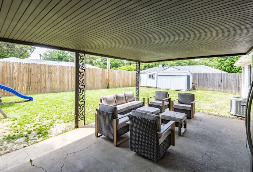 Covered patio with a concrete surface, featuring decorative metal columns and a slatted ceiling