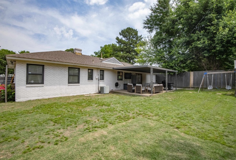 Expansive backyard featuring a covered patio, privacy fencing, mature trees, and a well-maintained lawn