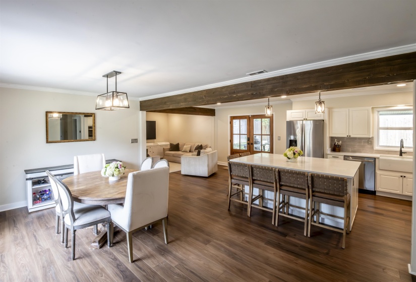 Open-concept living space featuring wood-finish flooring, a kitchen island with seating, white cabinetry, stainless steel appliances, and a farmhouse sink