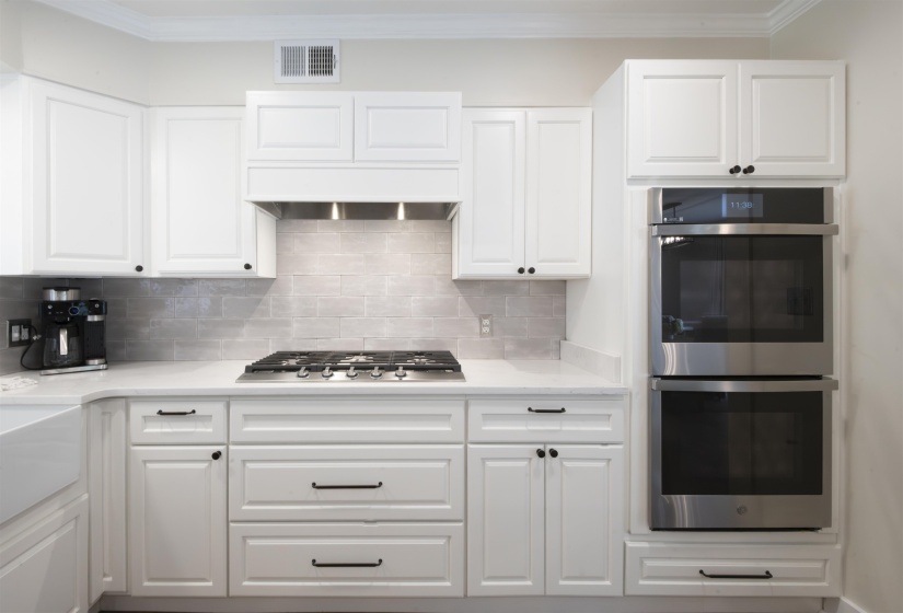 Modern kitchen featuring white shaker cabinetry, stainless steel double ovens, a gas range with a coordinating vent hood, and light-toned tile backsplash
