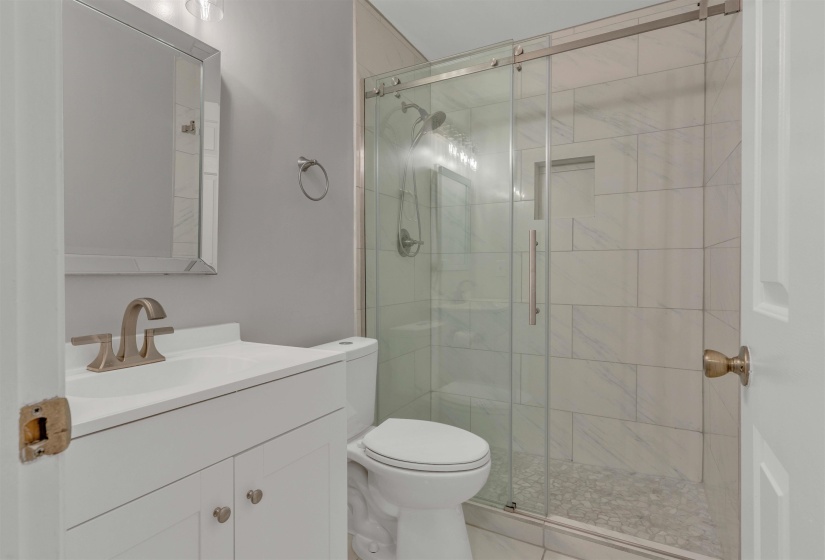 Bathroom featuring a frameless glass shower enclosure with subway tile surround and pebble tile flooring