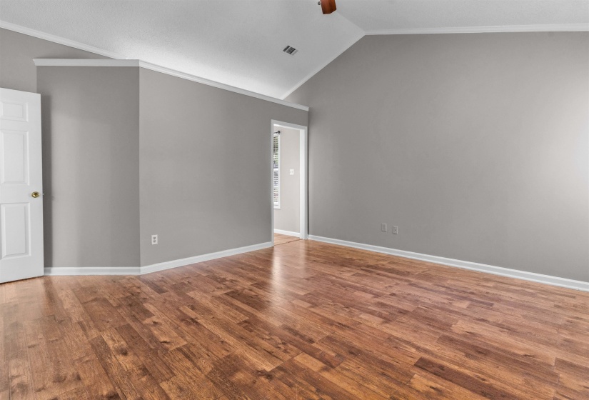 Spacious interior room featuring wood-finish flooring, vaulted ceiling, and neutral gray walls with white trim