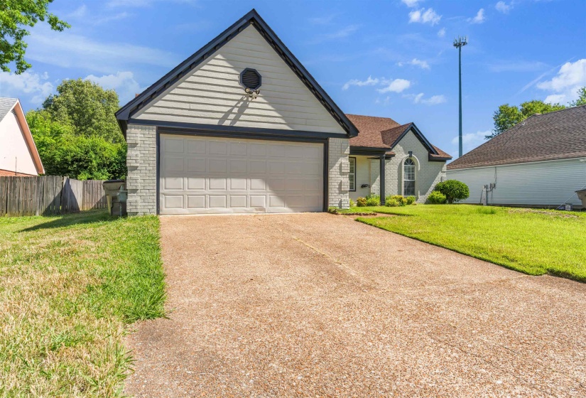 Single-story residence featuring a two-car garage with a panel door, a light-toned brick facade, and a pitched roof