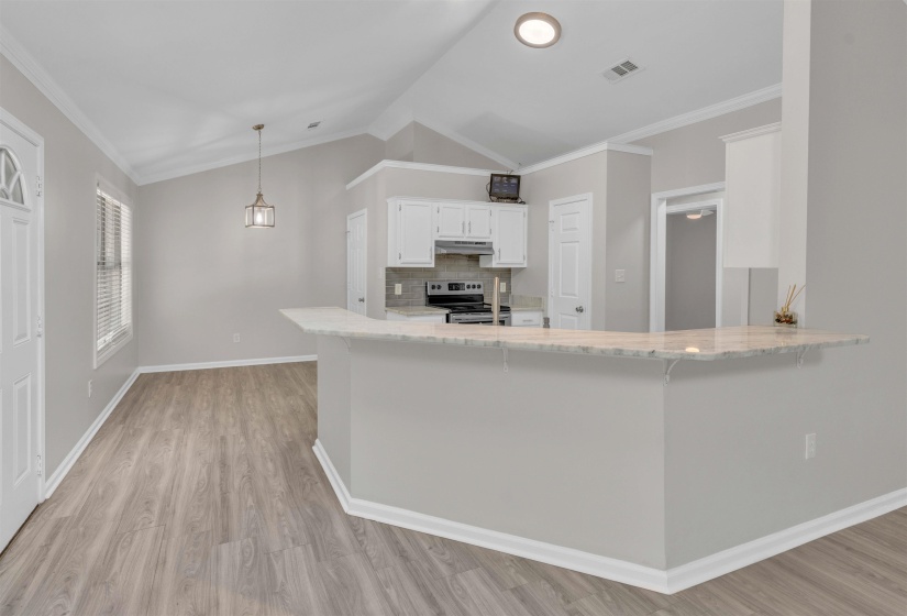 Open-concept living space featuring wood-finish flooring, vaulted ceilings, and a kitchen with white cabinetry
