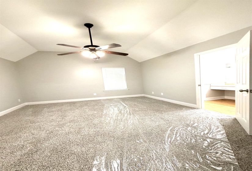 Vaulted ceiling with an installed ceiling fan, neutral wall paint, and gray carpeted flooring