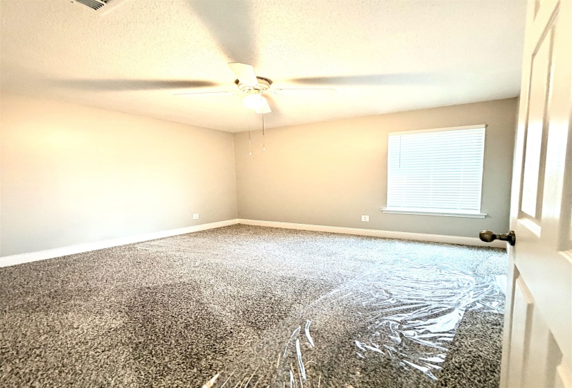 Carpeted room with a ceiling fan light fixture, natural light from a window with horizontal blinds, and a white baseboard trim