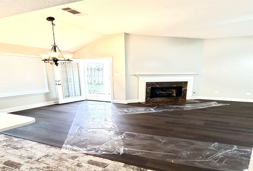 Vaulted ceiling living space featuring dark wood-finish flooring, a fireplace with a stone surround and white mantel, and French doors