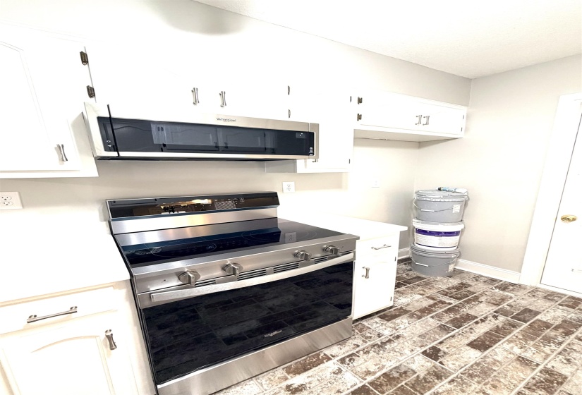 Kitchen featuring stainless steel range and microwave, white cabinetry with brushed nickel hardware, light countertops, and brick-patterned flooring