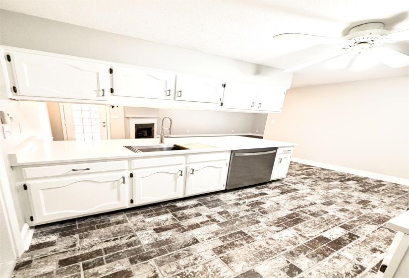 Kitchenette featuring white cabinetry, light-toned countertops, a stainless steel sink with a gooseneck faucet, a stainless steel dishwasher, and brick-patterned flooring