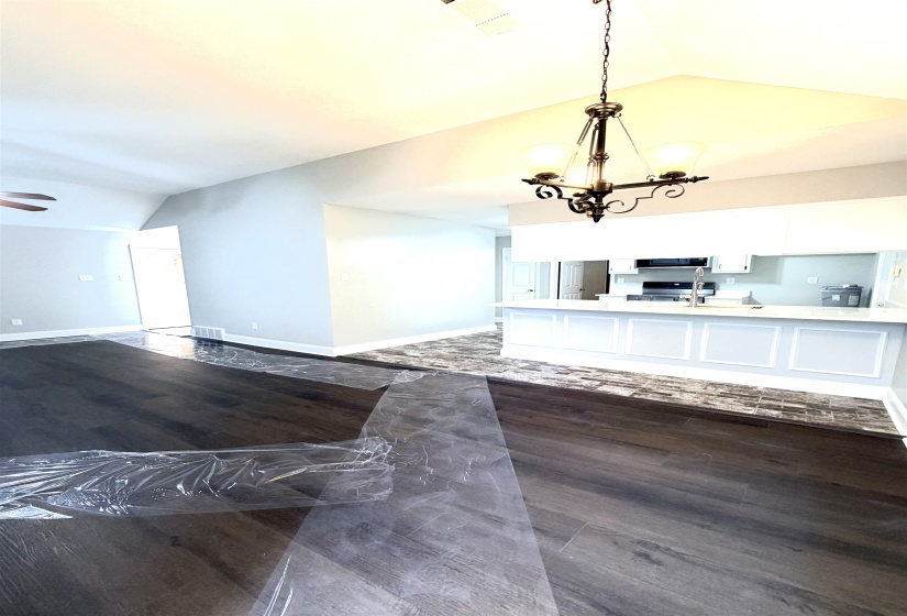 Vaulted ceilings with a decorative chandelier, dark wood-finish flooring, and a kitchen island featuring white cabinetry and a light-colored countertop