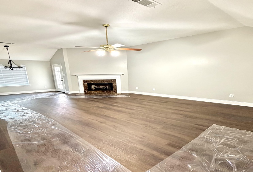 Spacious living area featuring vaulted ceilings, wood-finish flooring, a decorative fireplace with a stone surround, and an overhead ceiling fan