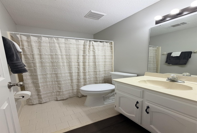 Bathroom featuring an integrated vanity sink with a white cabinet, tile flooring, a standard toilet, and a shower area