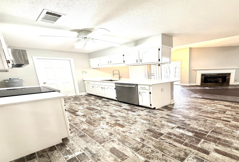 Kitchen featuring white cabinetry, a stainless steel dishwasher, a black electric cooktop, light countertops, and brick-patterned flooring