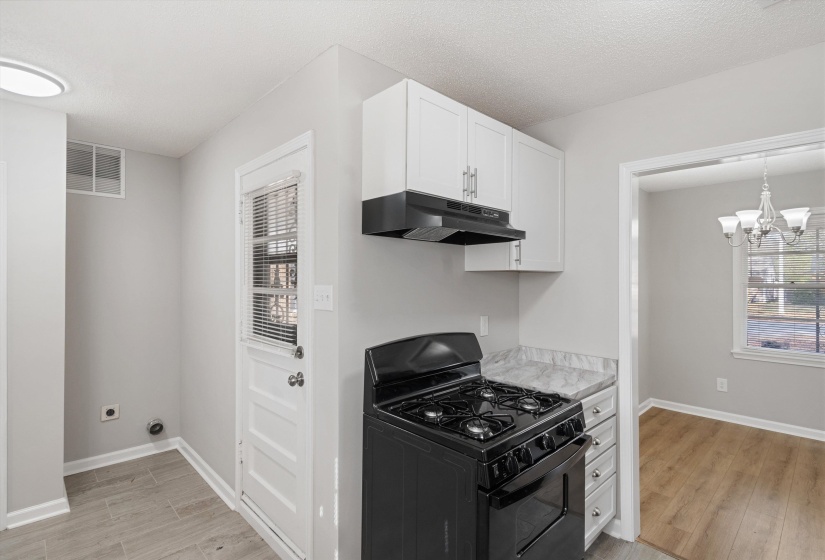 Kitchen with black gas range oven, light countertops, white cabinetry, a chandelier, and under cabinet range hood