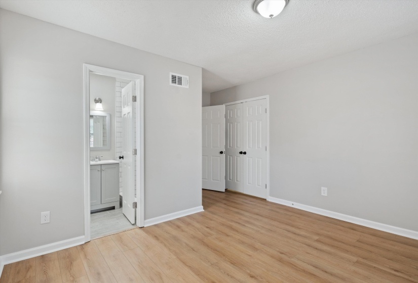Unfurnished bedroom featuring light wood finished floors, a textured ceiling, a closet, and ensuite bathroom