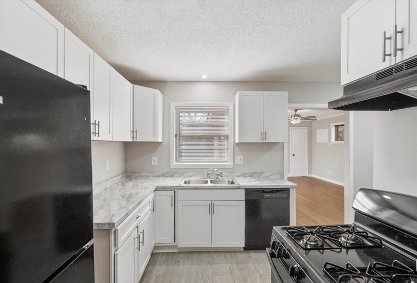 Kitchen featuring black appliances, light countertops, white cabinets, under cabinet range hood, and a textured ceiling
