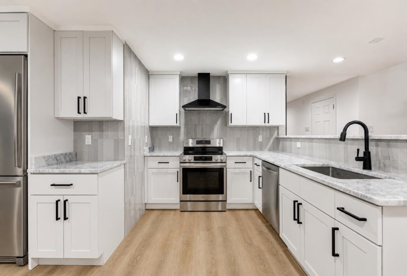 Modern kitchen featuring white shaker cabinetry, stainless steel appliances, light-toned wood-finish flooring, a matte black faucet, and a contemporary tile backsplash