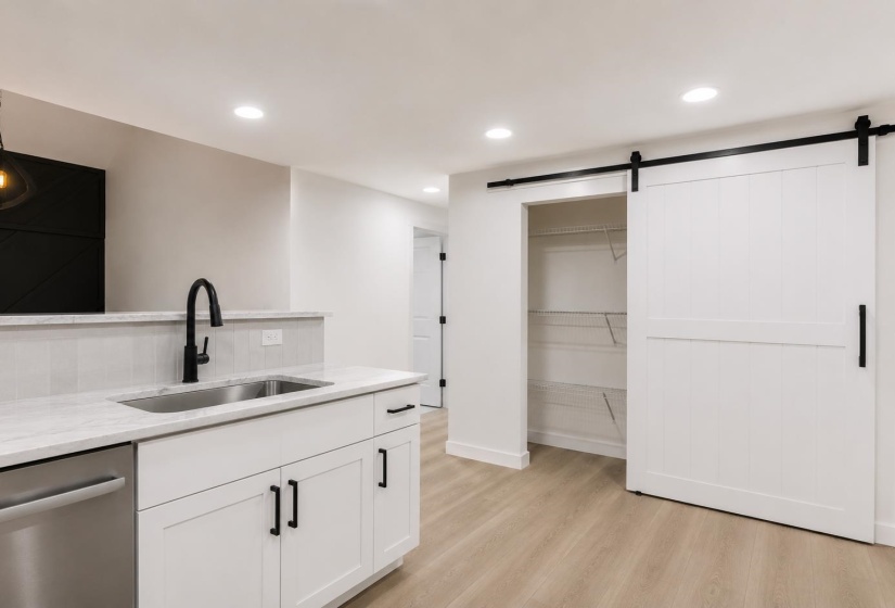 Kitchenette featuring a stainless steel sink with a matte black faucet, white shaker-style cabinetry, and light-toned countertops