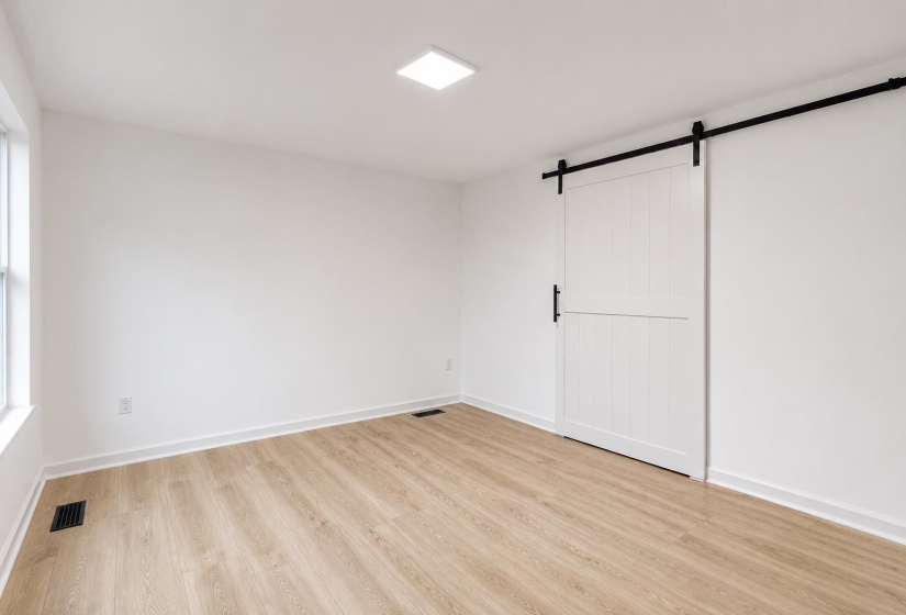 Spacious room featuring light wood-finish flooring, a white paneled barn door with black hardware, and a modern recessed ceiling light fixture