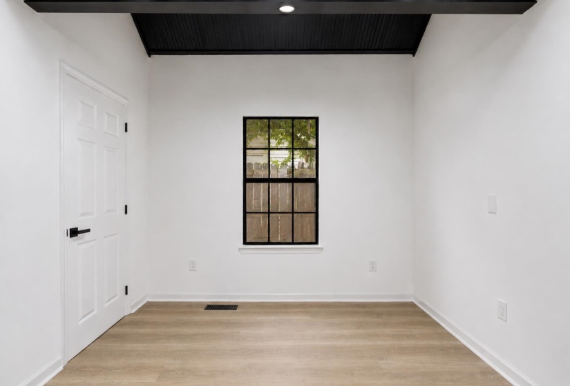 Bright interior space featuring light wood-finish flooring, a black grid window, and a white paneled door with matte black hardware