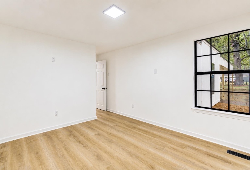 Room with light wood-finish flooring, white walls, and a large multi-pane window with black framing