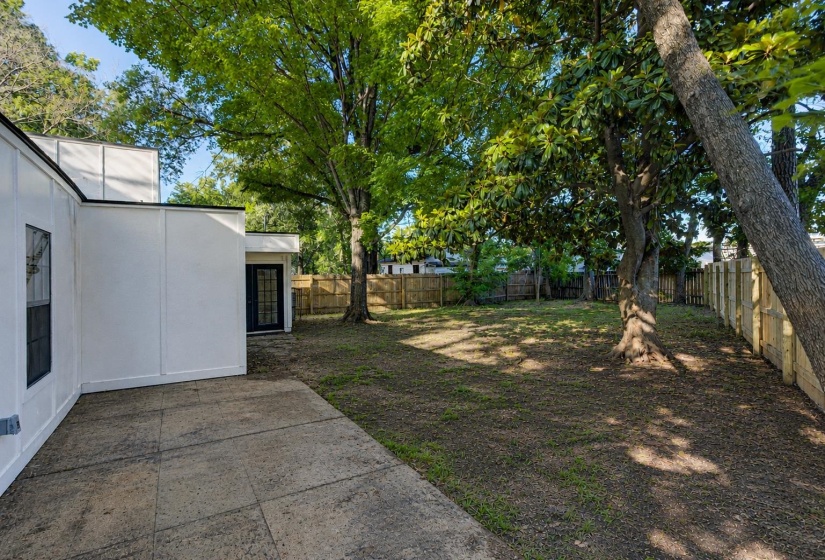 Spacious backyard featuring mature trees, a privacy fence, and a concrete patio