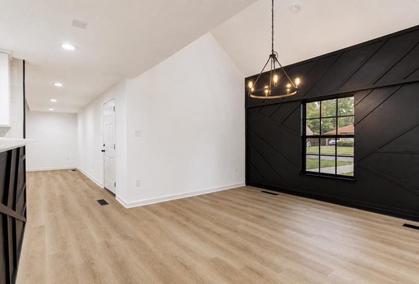 Vaulted ceiling with an industrial-style chandelier, contrasting black accent wall with applied molding, and light wood-finish flooring