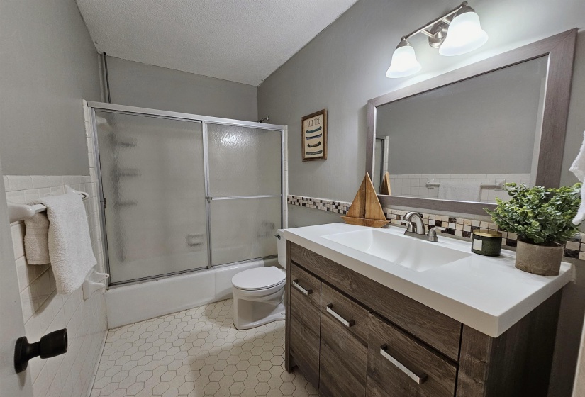 Bathroom with vanity, tile walls, bath / shower combo with glass door, light tile patterned floors, and a textured ceiling