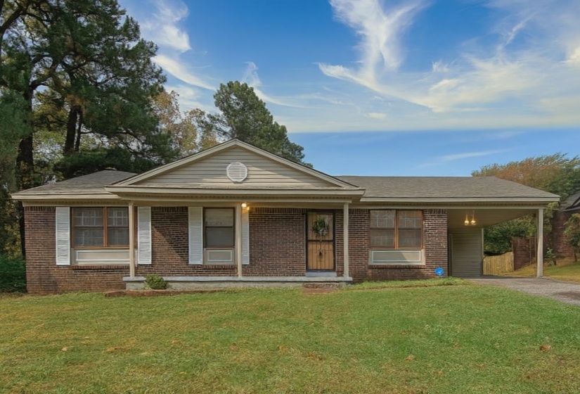 Single story home featuring covered porch, a front lawn, driveway, an attached carport, and brick siding