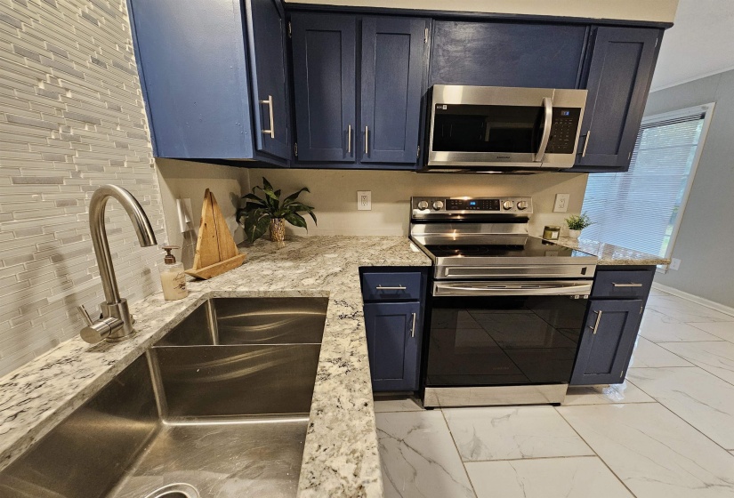 Kitchen featuring appliances with stainless steel finishes, light stone counters, light marble finish floors, and blue cabinets
