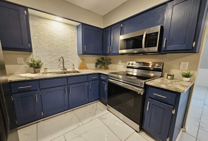 Kitchen featuring stainless steel appliances, light stone counters, light marble finish flooring, and blue cabinetry