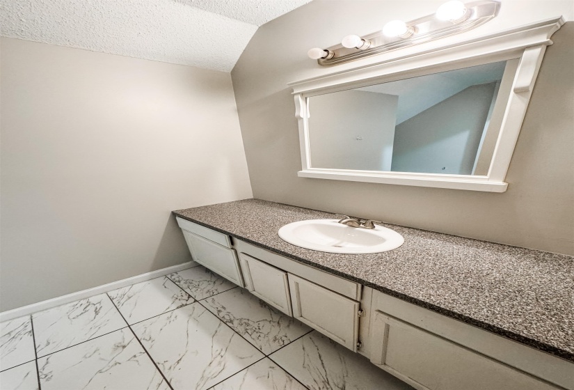 Bathroom featuring tile patterned floors, vanity, vaulted ceiling, and a textured ceiling