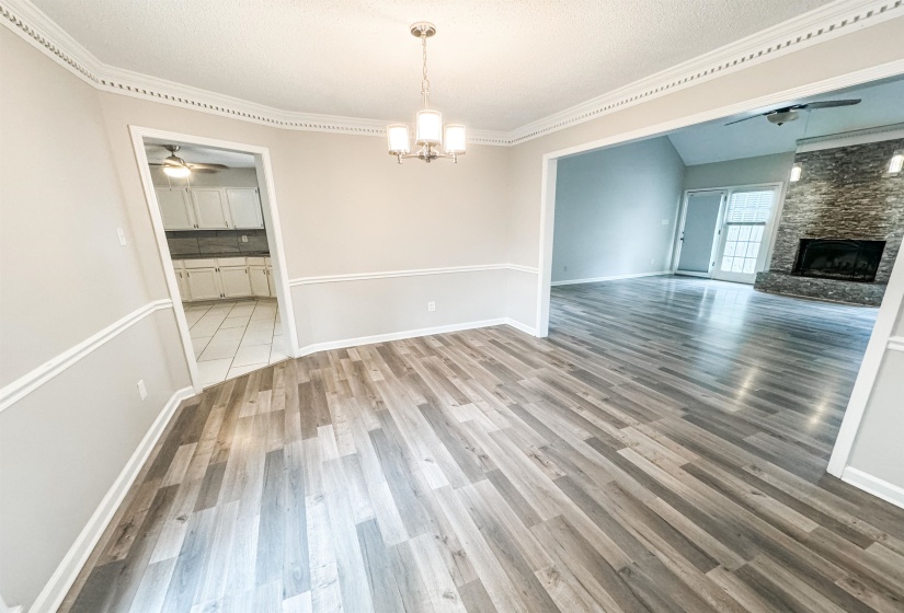 Unfurnished dining area featuring a textured ceiling, ceiling fan with notable chandelier, a stone fireplace, wood-type flooring, and ornamental molding