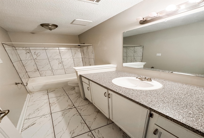 Full bathroom with a textured ceiling, toilet, tile patterned floors, vanity, and shower / tub combination