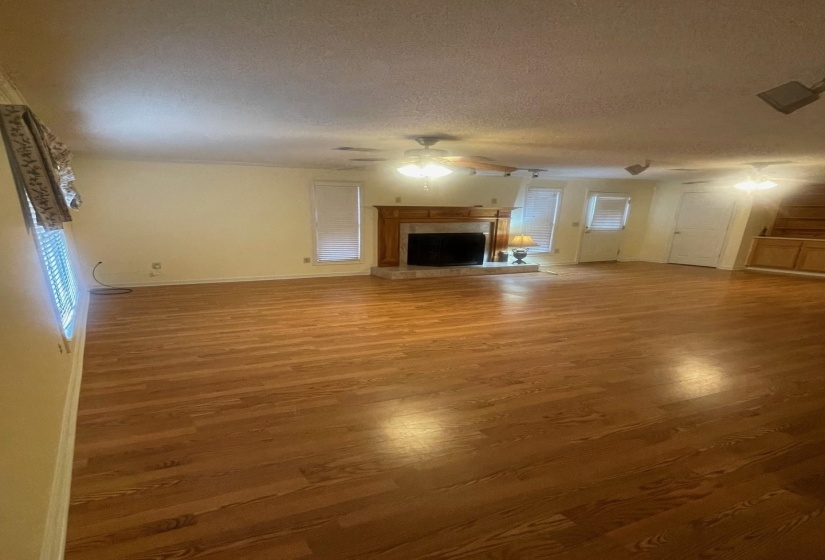 Spacious room featuring wood-finish flooring, a fireplace with a wood mantle and stone surround, and multiple windows with blinds