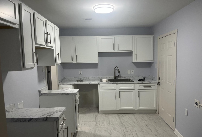 Kitchen with white cabinetry, light countertops, and light marble finish flooring