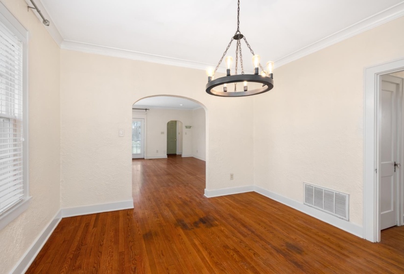 Unfurnished dining area featuring arched walkways, crown molding, dark wood-style flooring, and a chandelier