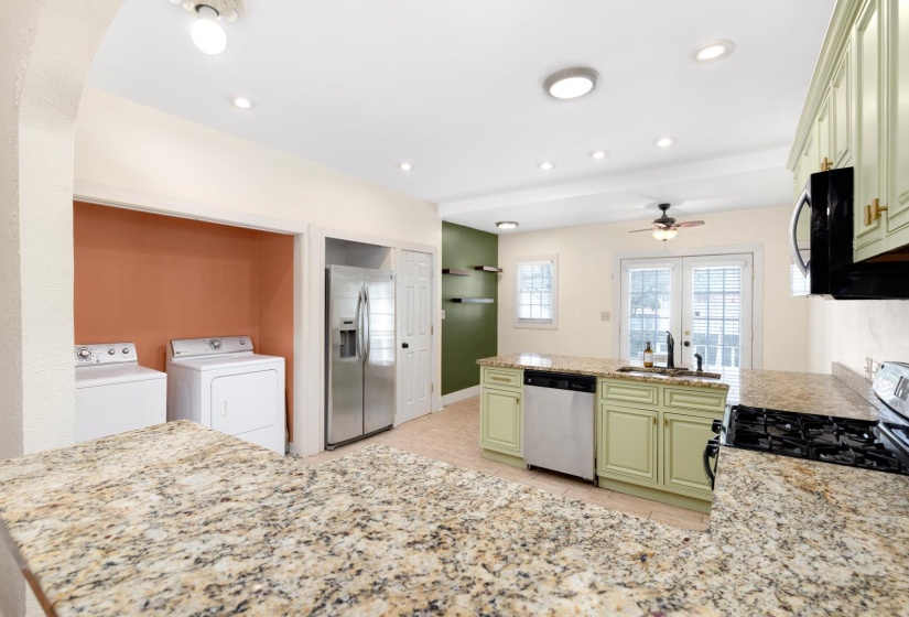 Kitchen featuring a peninsula, stainless steel appliances, light stone counters, washer and clothes dryer, and green cabinets