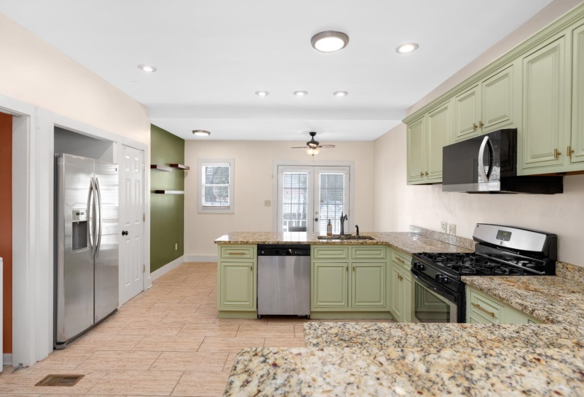 Kitchen with green cabinetry, stainless steel appliances, a peninsula, light stone countertops, and a ceiling fan