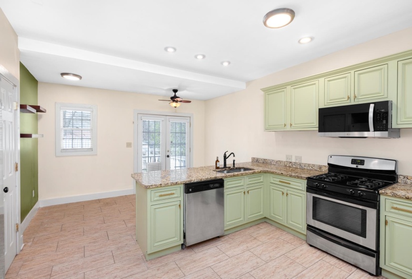 Kitchen with green cabinets, stainless steel appliances, a peninsula, light stone countertops, and ceiling fan