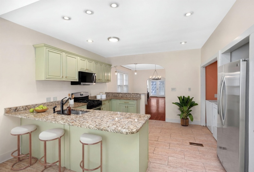 Kitchen featuring green cabinetry, a peninsula, wood finish floors, light stone counters, and stainless steel appliances
